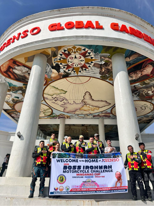 Participants and organizers gather at the 2026 BOSS Ironman Checkpoint at the AGG, featuring a prominently displayed event tarpaulin. The checkpoint serves as a designated stop for riders during the endurance event, highlighting support and coordination for the 2026 BOSS Ironman.